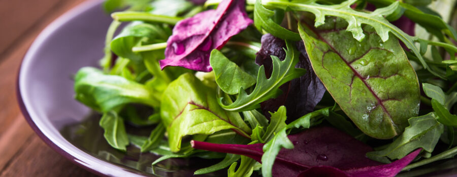 Fresh salad with mixed greens (arugula, mesclun, mache) on dark wooden background close up. Healthy food.